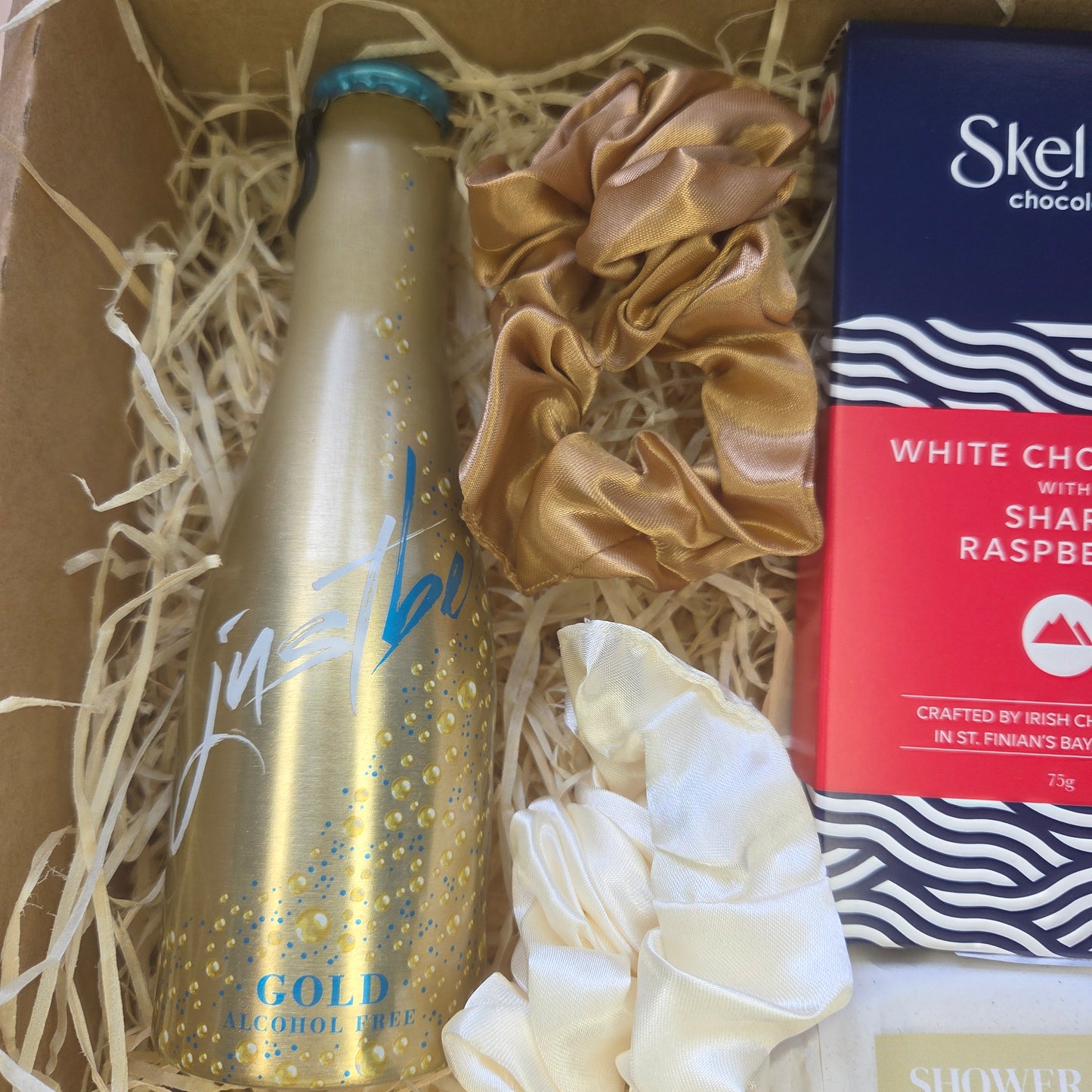 Gold bottle with decorative packaging including a box and gloves on a straw-lined surface.