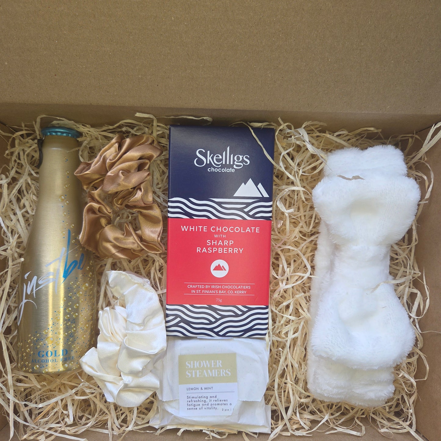 Gift box with Skelligs white chocolate and raspberry bar, gold bottle, and decorative items.