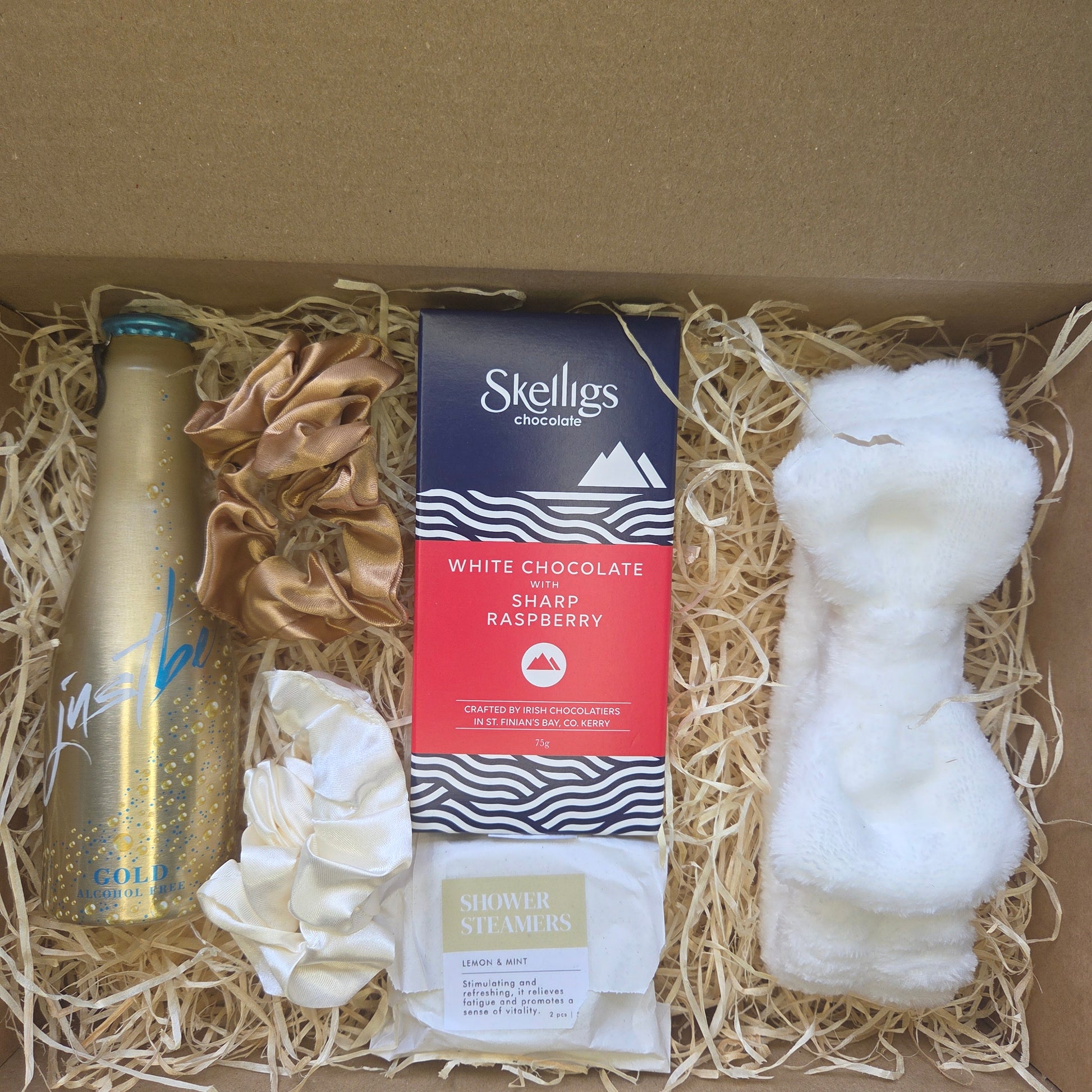 Gift box with Skelligs white chocolate and raspberry bar, gold bottle, and decorative items.