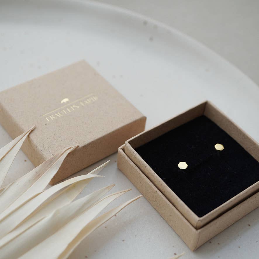 A pair of small gold hexagonal stud earrings displayed in an open black-lined jewelry box.