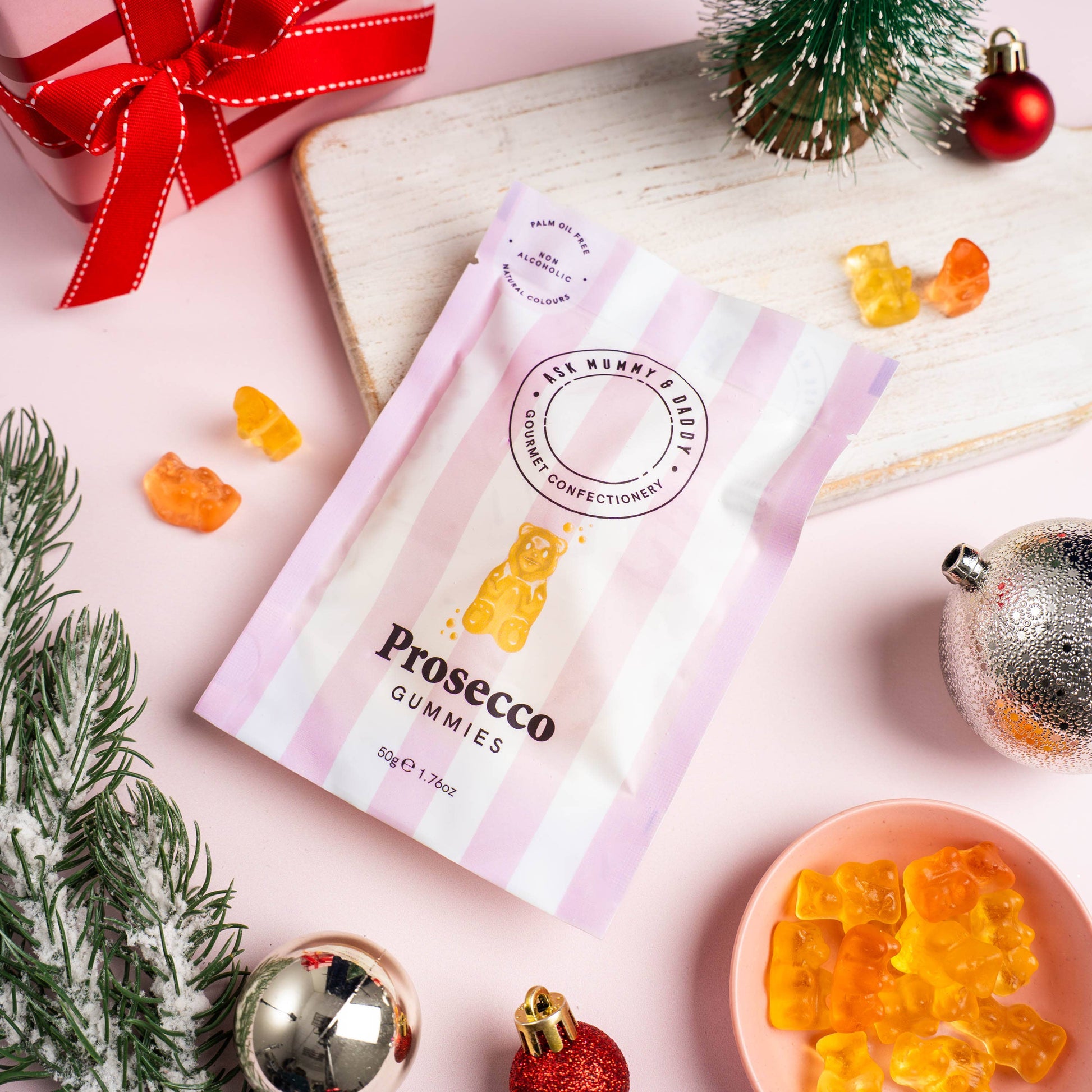 Prosecco gummy bears packaging with gummies and Christmas decorations on a pink surface