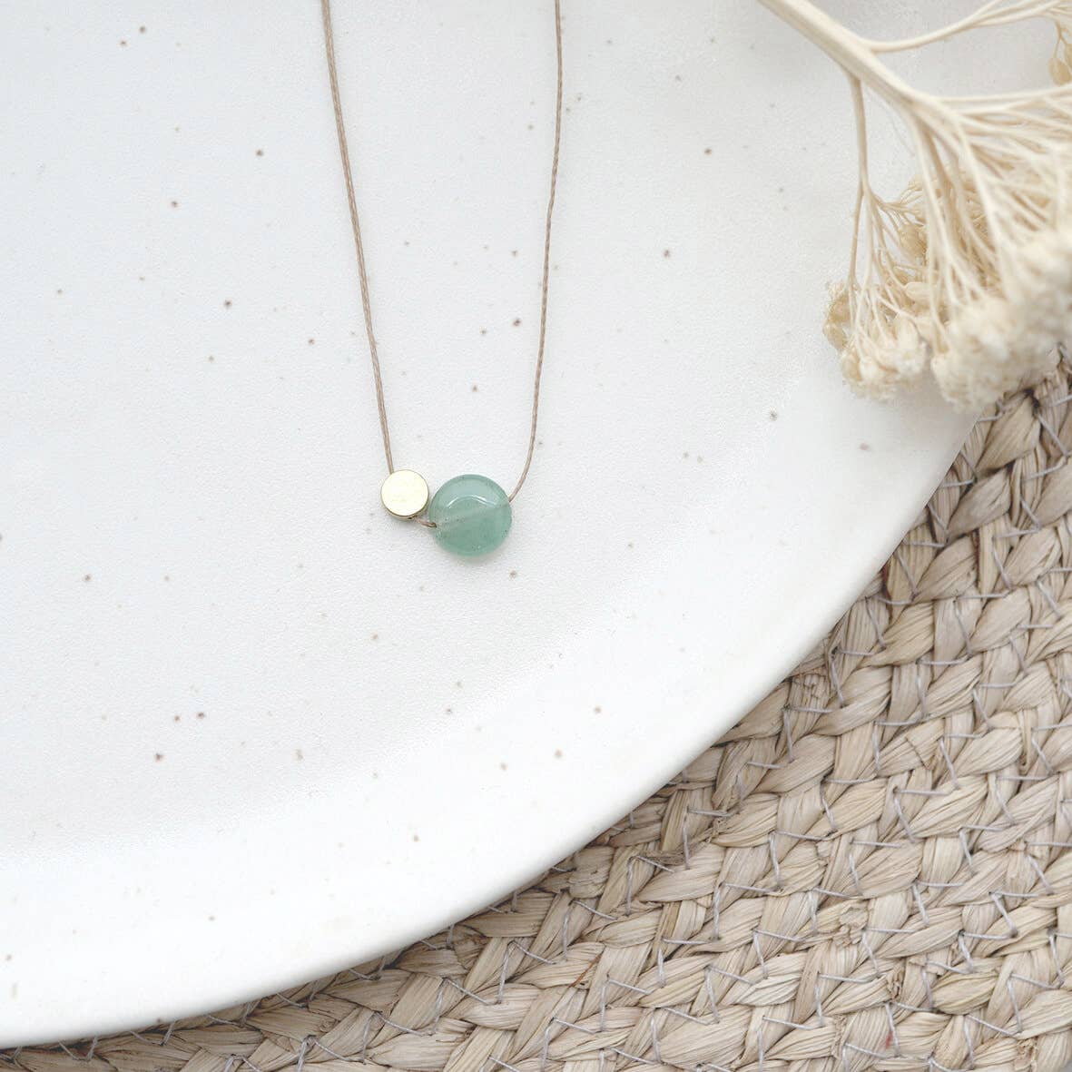 Necklace with a green bead on a white surface with dried plants