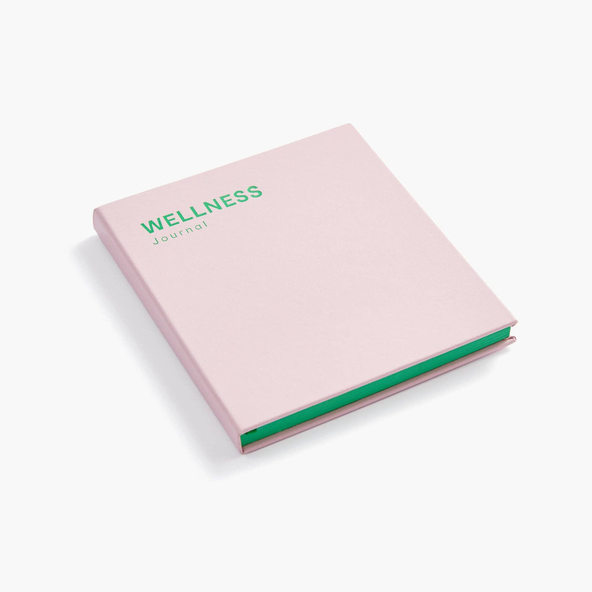 A light pink hardcover journal with the words 'WELLNESS journal' printed in green on the cover, shown at an angle on a light gray background.